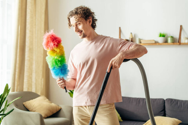 Een knappe man in knusse huiskleding houdt gelukkig een heldere, kleurrijke stofdoek vast. - Foto, afbeelding