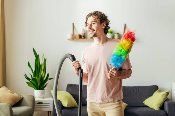 Un uomo elegante che tiene un giocattolo colorato accanto a un aspirapolvere in una casa accogliente. - Foto, immagini