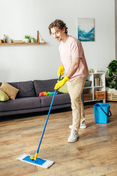 Egy jóképű férfi otthonos viseletben szorgalmasan felmossa a padlót.. - Fotó, kép