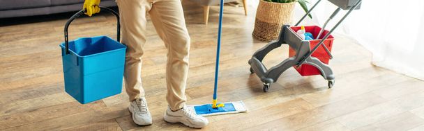 Muž v útulných domácích šatech pilně utírá podlahu. - Fotografie, Obrázek