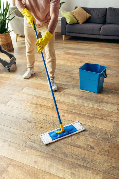 Hezký muž v útulném domácím oblečení pilně utírá podlahu. - Fotografie, Obrázek