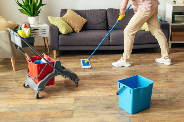 Ein Mann in Aktion, der in gemütlicher häuslicher Umgebung den Boden mit einem Wischmopp reinigt. - Foto, Bild