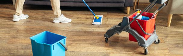 Hezký muž v útulném domácím oblečení používá mop k čištění podlahy. - Fotografie, Obrázek