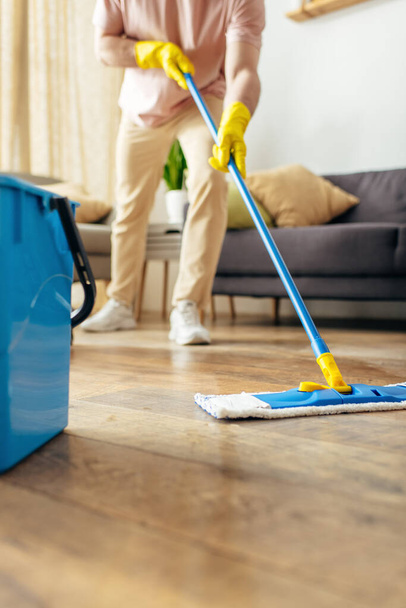 Un bell'uomo in casalinghe accoglienti pulisce diligentemente il pavimento. - Foto, immagini