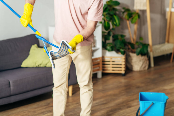 Egy férfi otthonosan öltözködő szakszerűen kitakarítja a nappalit egy felmosóval.. - Fotó, kép