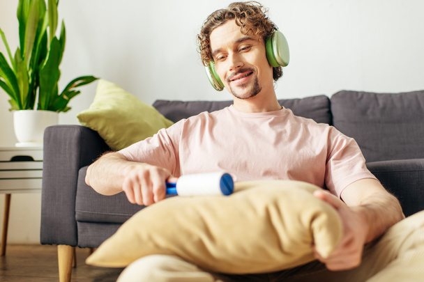 Beau homme dans des vêtements confortables appréciant la musique près du canapé avec écouteurs. - Photo, image
