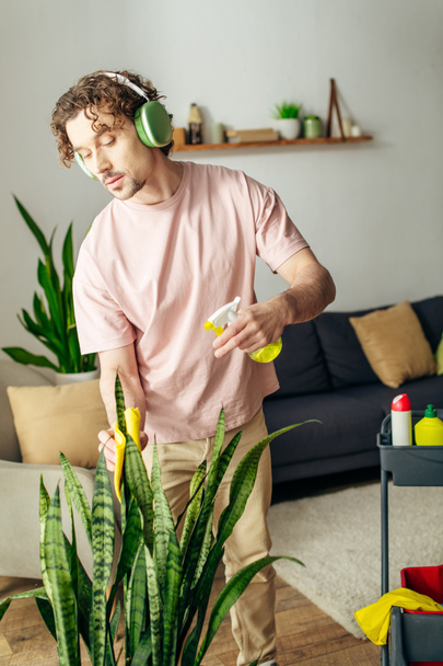 Чоловік у затишному домашньому вбранні стоїть перед рослиною, в навушниках. - Фото, зображення