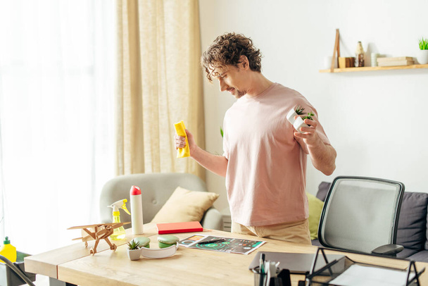 Hombre guapo en ropa de casa acogedora sosteniendo un spray en una sala de estar. - Foto, imagen