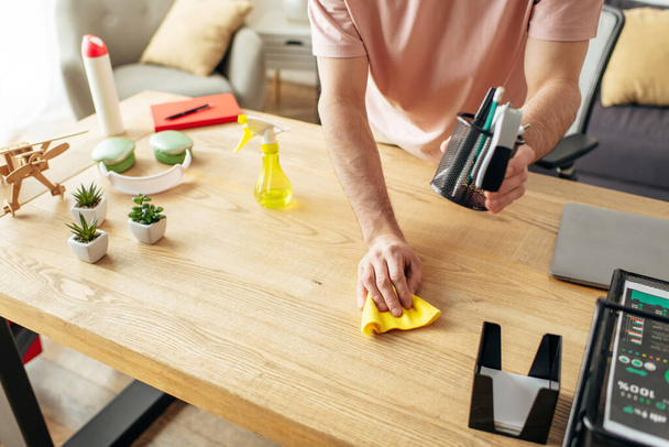 Jóképű férfi kényelmes otthonban szorgalmasan tisztítja az asztalt egy szivaccsal. - Fotó, kép