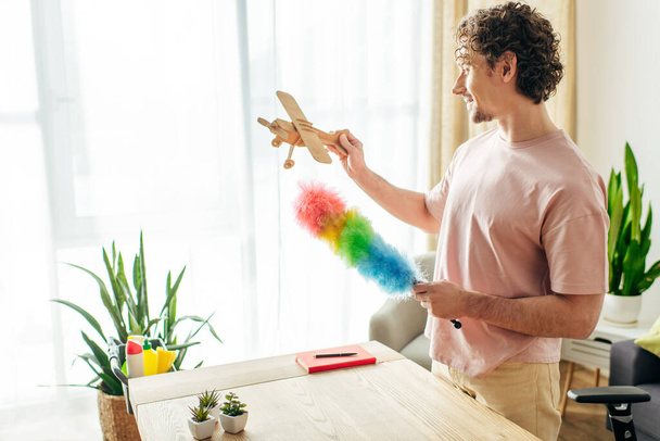 Мужчина в уютной домашней одежде играет с игрушечным самолетом во время уборки дома. - Фото, изображение