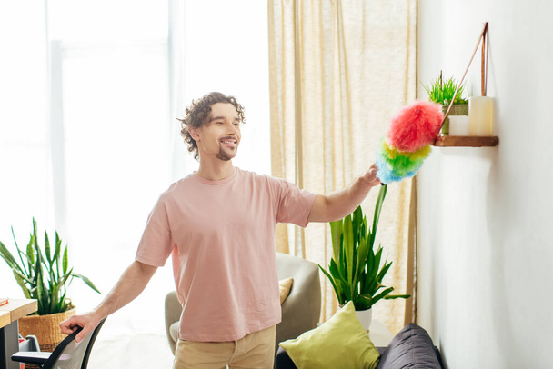 Όμορφος άντρας σε άνετο σπίτι φορώντας ένα πολύχρωμο ξεσκονόπανο. - Φωτογραφία, εικόνα