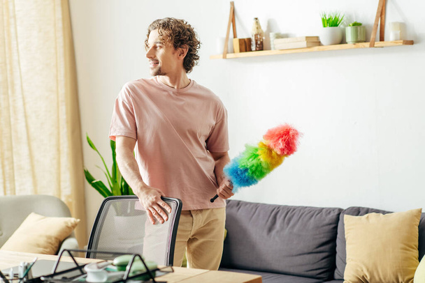 Ein stilvoller Mann putzt das Wohnzimmer mit einem Staubwedel. - Foto, Bild