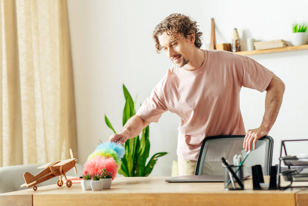 Homem elegante em casa camisa rosa limpeza com espanador dentro de casa. - Foto, Imagem