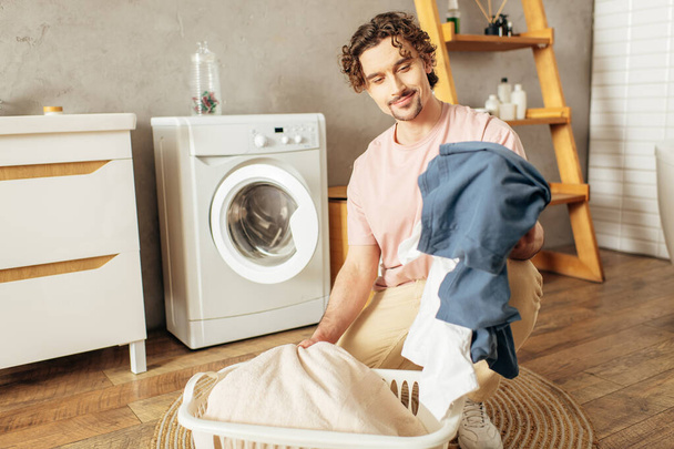 Mies kotoisissa kotivaatteissa pitää pyykkipussia pesukoneen edessä.. - Valokuva, kuva