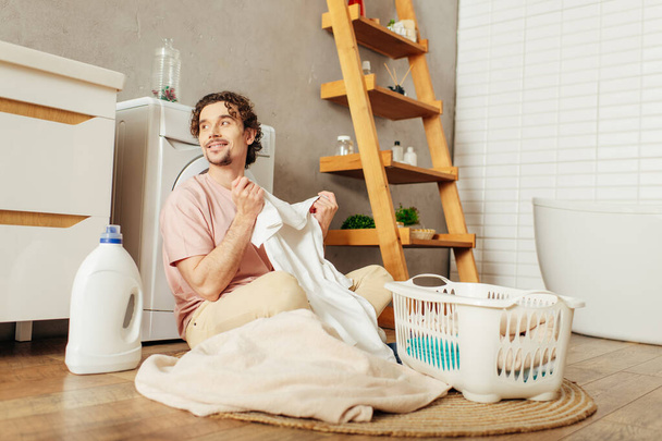 Ev elbiseli yakışıklı bir adam yerde oturmuş çamaşırları sıralıyor.. - Fotoğraf, Görsel