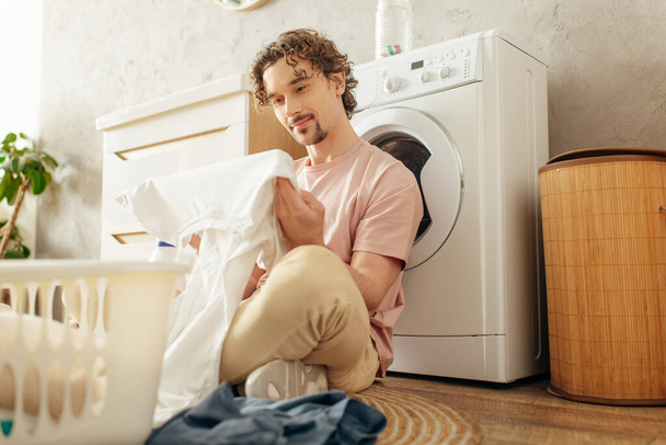 Een man in knusse huiskledij zit naast een wasmachine in een schoonmaak spree. - Foto, afbeelding