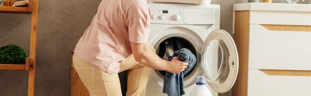 Ein Mann legt Kleidung vorsichtig in eine Waschmaschine. - Foto, Bild