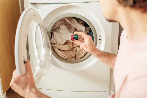 Ein gutaussehender Mann in gemütlicher Hauskleidung, der Waschmittel in die Waschmaschine gibt. - Foto, Bild