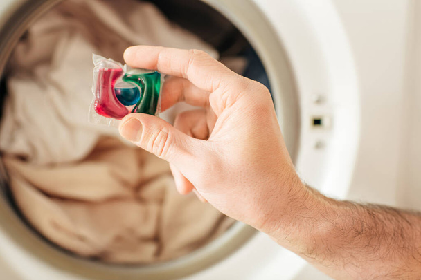A hand holding a detergent in front of a washing machine. - Photo, Image