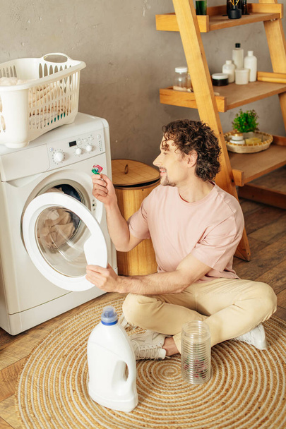Un hombre en ropa de casa acogedora se sienta al lado de una lavadora. - Foto, imagen