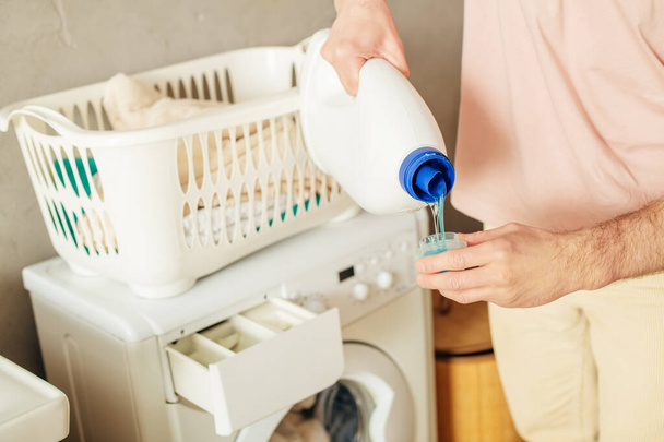 Homem bonito em roupa de casa aconchegante derramando detergente na máquina de lavar roupa. - Foto, Imagem