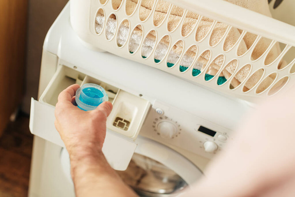 Красивий чоловік у затишному домашньому одязі завантажує пральний порошок у пральну машину. - Фото, зображення