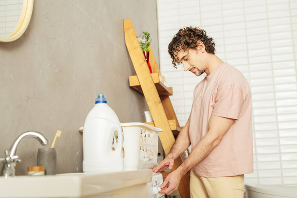 Um homem bonito em roupa de casa aconchegante lavando suas roupas. - Foto, Imagem