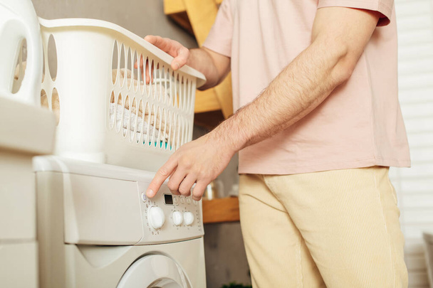 Schöner Mann in kuscheliger Homewear stellt Wäschekorb auf Waschmaschine. - Foto, Bild