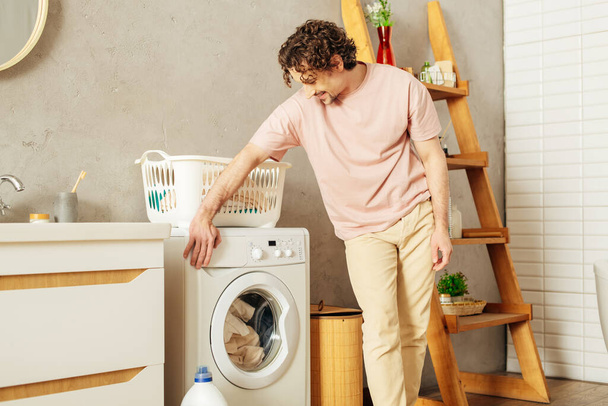 居心地の良いホームウェアのハンサムな男は洗濯機の隣に立っています. - 写真・画像