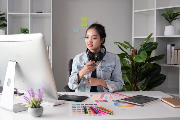 Grafik tasarımı yaparken kulaklık takan bayan tasarımcı masadaki bilgisayarla çalışmak için renk seçin.. - Fotoğraf, Görsel