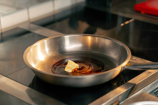 close-up στην επαγγελματική κουζίνα ο σεφ χρησιμοποιεί ένα μαχαίρι για να διανείμει λάδι σε ένα τηγάνι - Φωτογραφία, εικόνα