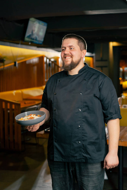 in een restaurant staat chef-kok in een zwart jasje lachend met een voorbereide salade - Foto, afbeelding