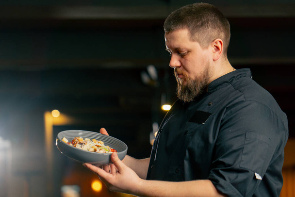 primer plano en un chef de restaurante en una chaqueta negra está sonriendo con una ensalada preparada - Foto, imagen