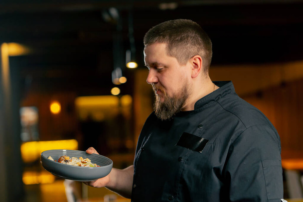 primer plano en un chef de restaurante en una chaqueta negra está sonriendo con una ensalada preparada - Foto, imagen