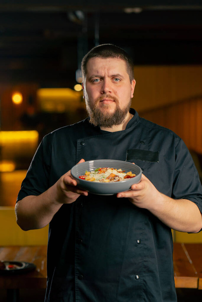 крупним планом в ресторані шеф-кухаря в чорній куртці стоїть з підготовленим салатом - Фото, зображення