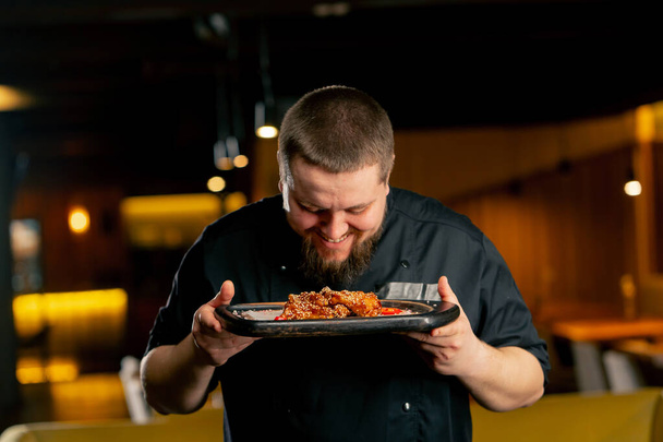 fechar um chef em preto em um restaurante cheira as asas de frango que ele próprio preparou - Foto, Imagem