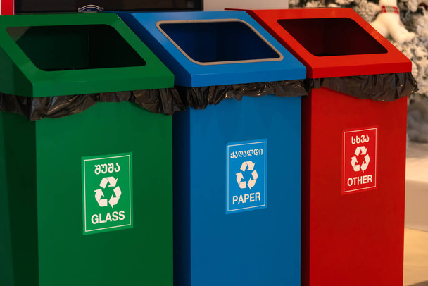Primo piano di bidoni della spazzatura verdi, blu e rossi per il dumping separato di vetro, carta e altri rifiuti nel negozio. Concetto di smaltimento corretto dei rifiuti. - Foto, immagini