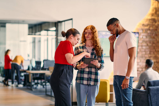A group of young business individuals, including a girl with orange hair and an African American man, stands in a modern corporate hallway, collectively examining business progress on a smartphone - Fotó, kép
