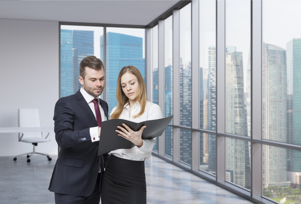 A young business couple are looking at the black document case in a modern panoramic office. Singapore cityscape. A concept of the teamwork. - Foto, Bild