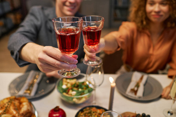Focus su due bicchieri di vino rosso tenuti da giovane tifo uomo e donna seduti a tavola serviti con cibo fatto in casa preparato per gli ospiti - Foto, immagini