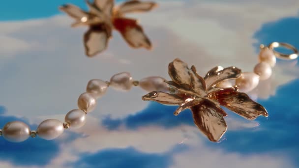 Nenhuma pessoa macro closeup de propaganda de brinco de flor dourada vintage elegante deitado por pulseira de pérola em abstrato fundo branco e azul no estúdio - Filmagem, Vídeo
