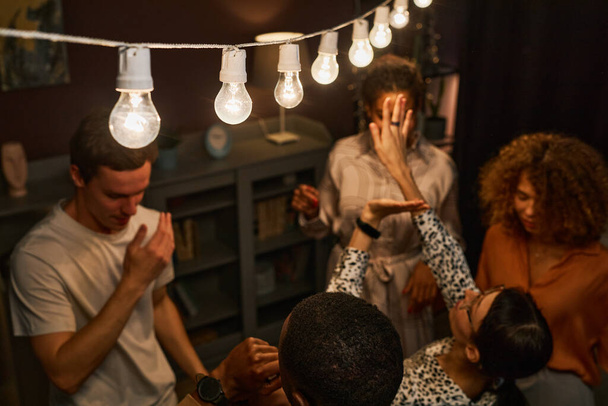 Focus op rij lichten lichtgevende kamer met groep extatische jonge interculturele vrienden dansen samen thuis feest of nachtclub - Foto, afbeelding