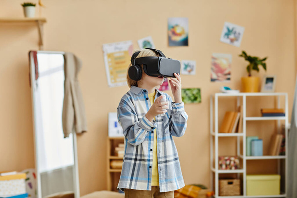 Iskolásfiú a casualwear és vr headset áll a kamera előtt otthoni környezetben, és játszani az új játék, miközben élvezi a szabadidő - Fotó, kép