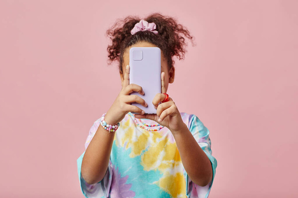 Afroamerikanerin hält Smartphone vor ihr Gesicht und schaut auf Bildschirm, während sie Selfie macht oder im Videochat kommuniziert - Foto, Bild