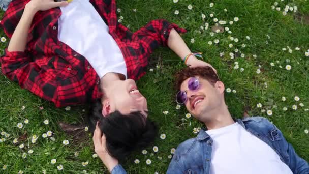 Relaxed gay couple, a Latino and a Chinese man, in a lush park with LGBT bracelets, celebrating diversity. - Footage, Video