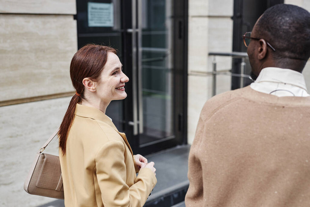 Giovane donna d'affari sorridente in formalwear beige guardando collega maschio afroamericano mentre discute con lui i punti di lavoro - Foto, immagini