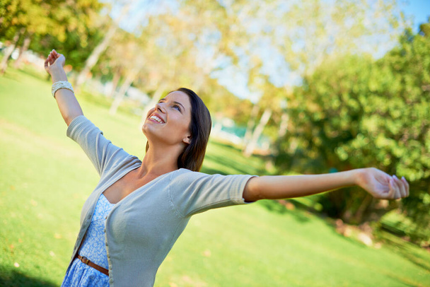 Happy woman, freedom and park for outdoor wellness, travel and fresh air in green environment and summer. A young and casual person stretching her arms, celebration and excited with energy in nature. - Photo, Image