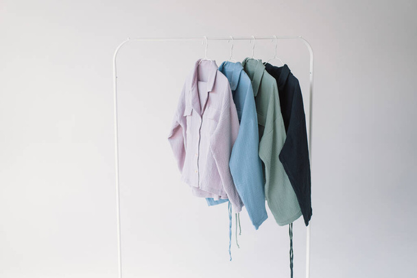 Una colección de ropa de colores en diferentes tonos de rosa claro a azul oscuro se muestra en un estante de ropa de metal. - Foto, imagen