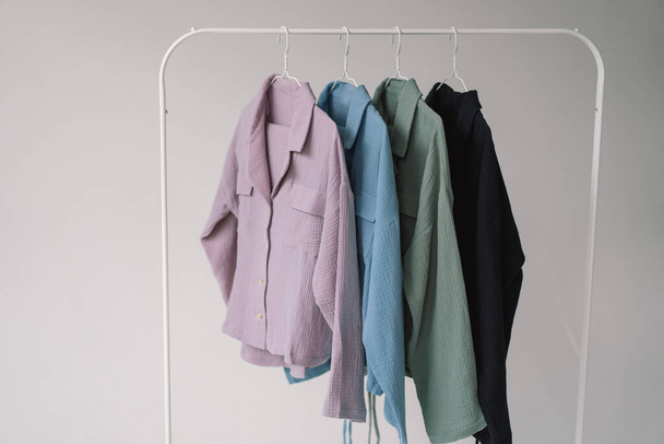 Una colección de ropa de colores en diferentes tonos de rosa claro a azul oscuro se muestra en un estante de ropa de metal. - Foto, imagen