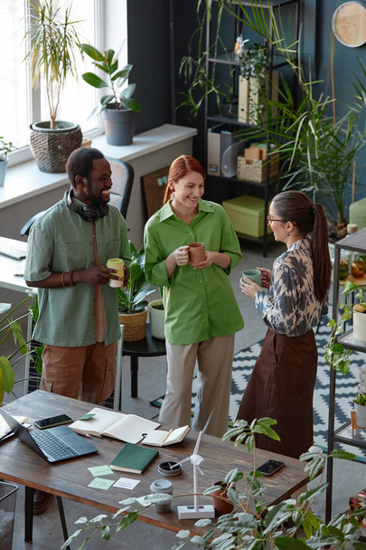 Вертикальний портрет творчої команди з трьох людей, які сміються під час спілкування стоячи в сучасному офісі під час перерви на каву - Фото, зображення